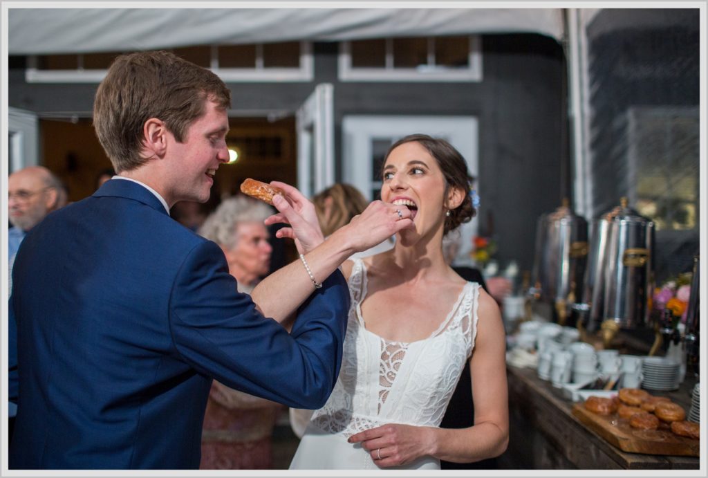 Katie and James' Hidden Pond Wedding | Bride and groom link arms and share donuts